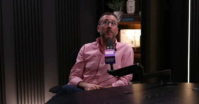 Judd Hoffman in a pink shirt speaking into a Fargo Talks microphone in a dark wood-panelled studio, mid-conversation.